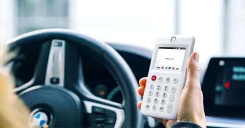 Taxichauffeur houdt een myPOS Go 2 pinapparaat vast achter het stuur van de auto